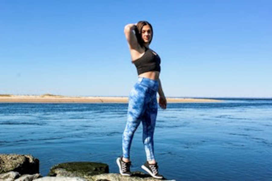 Woman standing on rocks by the water with hand on head