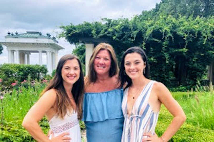 Mom with arms around two daughters standing outside and smiling