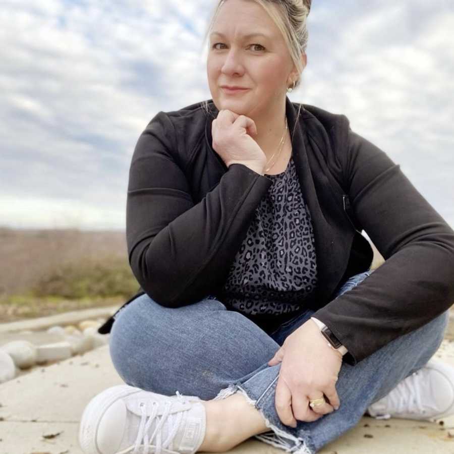 Woman sitting cross-legged outside wearing black jacket