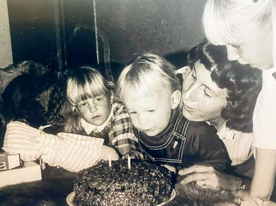 Black and white photo of mother with two daughters blowing out candles on a birthday cake