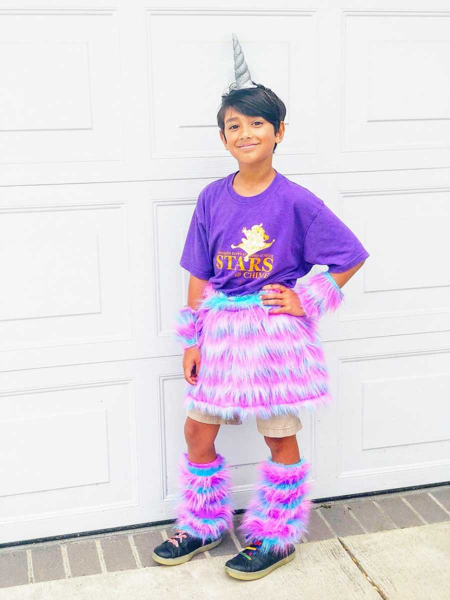 A boy wears a purple shirt and a fuzzy pink skirt