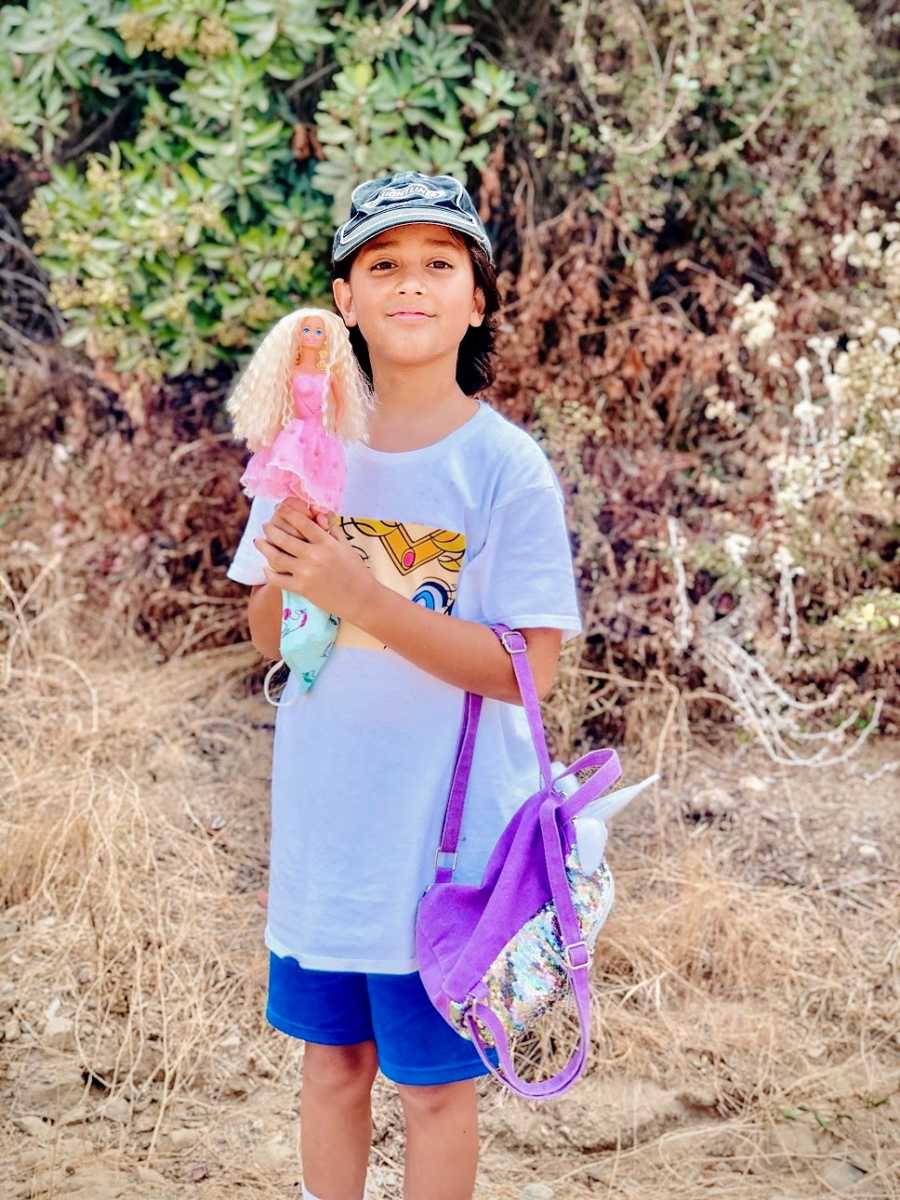 A boy with a sparkly backpack holds up a doll