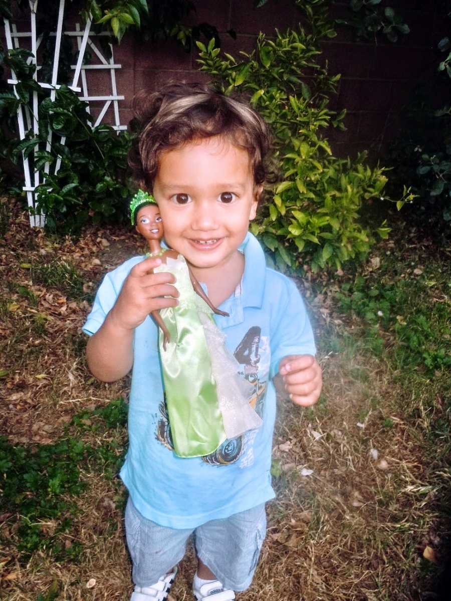 A toddler holds up a Princess Tiana doll