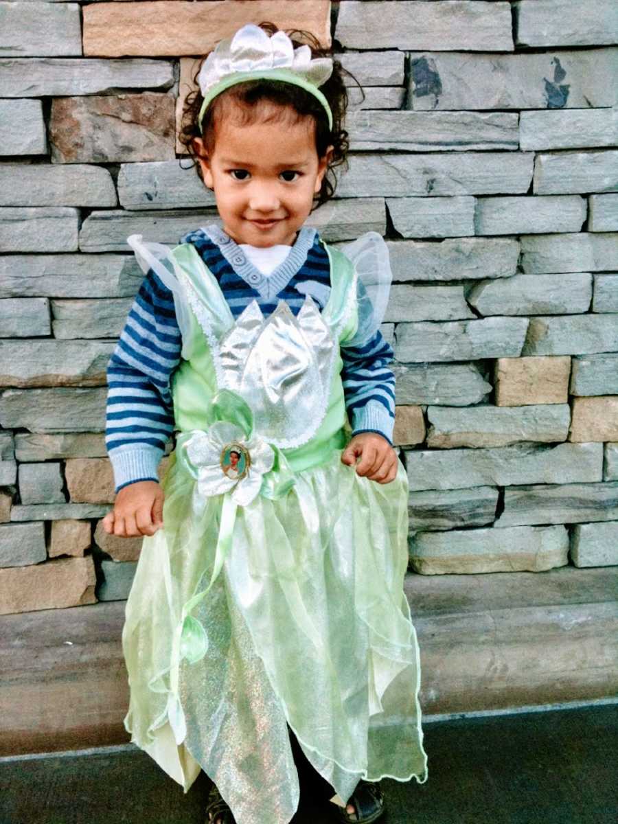 A little boy wearing a green princess dress and tiara