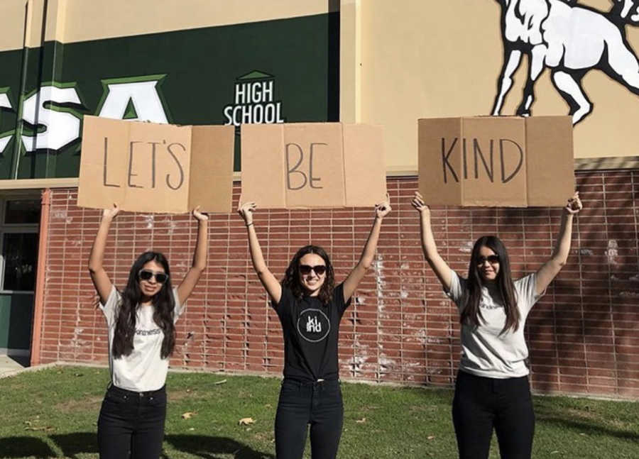 three girls with signs that spell out let's be kind