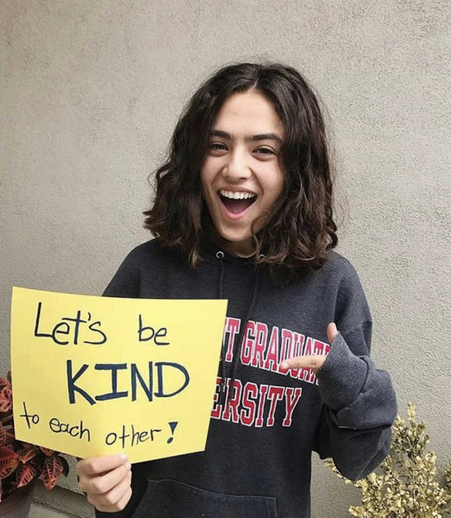 girl pointing to a sign saying let's be kind