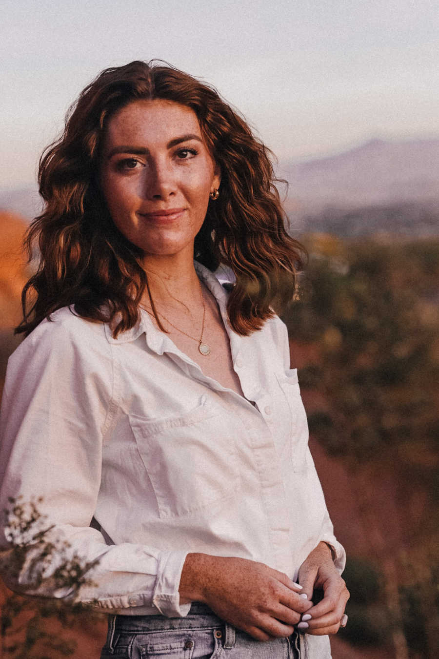 Woman standing outside wearing button-up shirt smiling