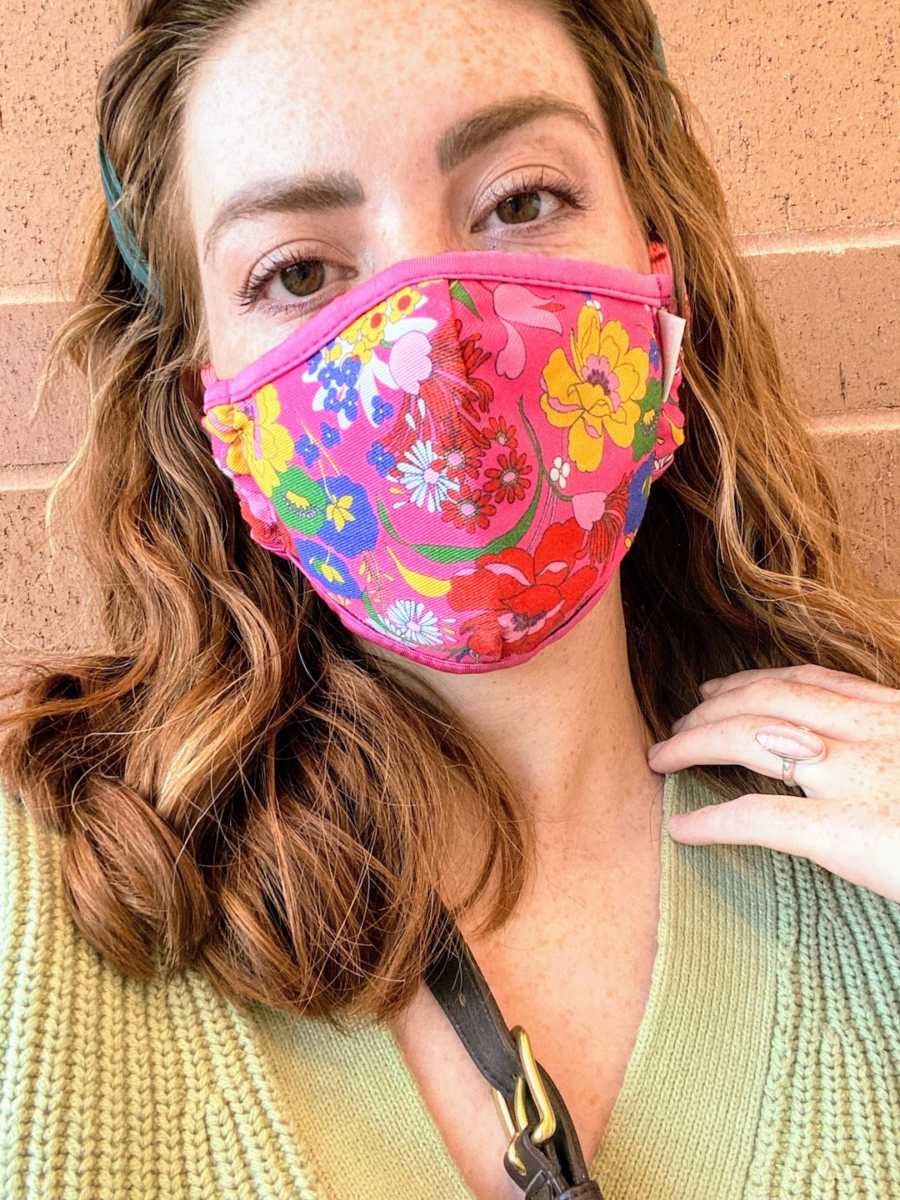 Woman wearing floral face mask in front of brick building