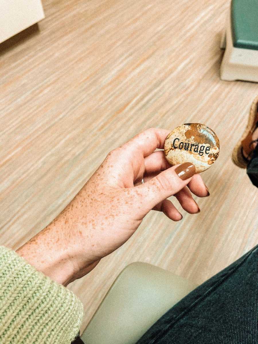 Woman's hand holding brownstone that says "courage"