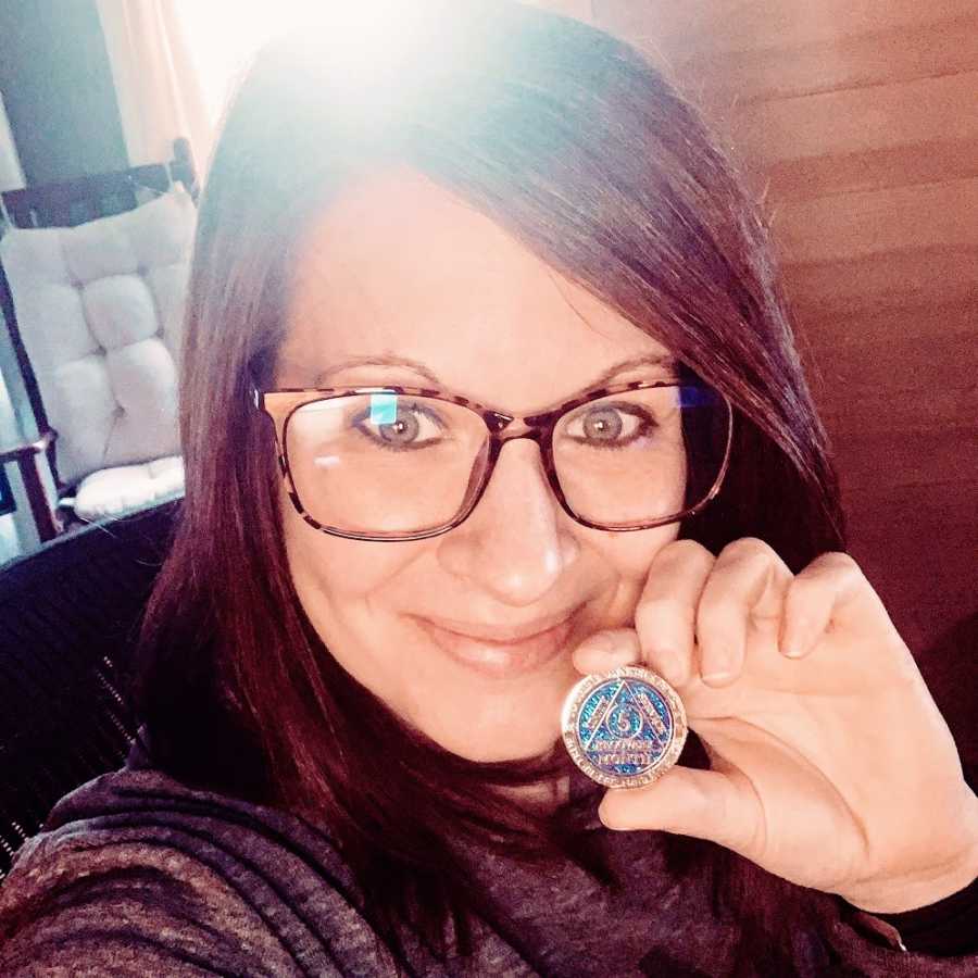 A recovering alcoholic holds up her sobriety chip