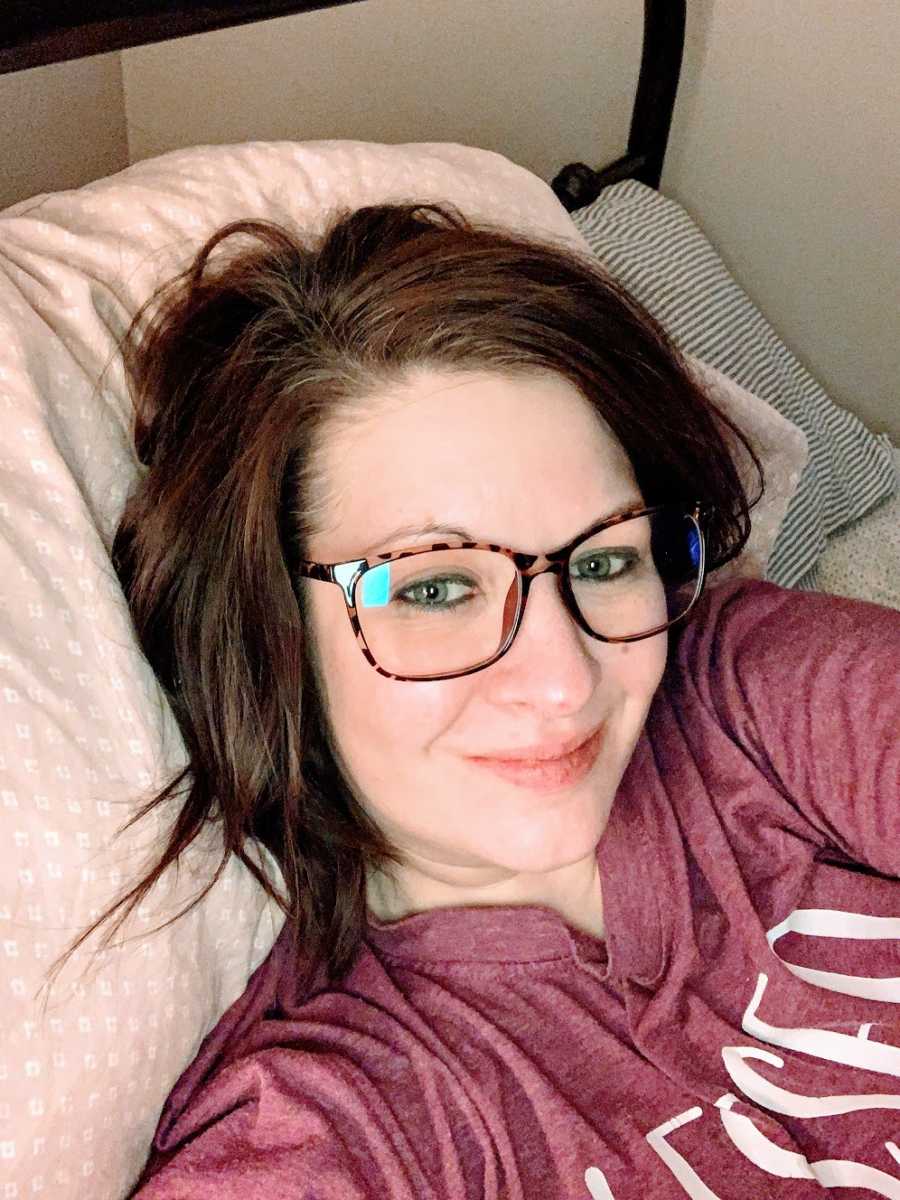 A recovering alcoholic lies in her bed wearing glasses