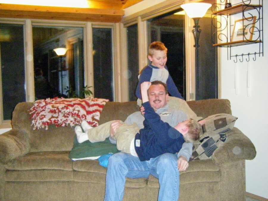 Father sitting on couch with one son on lap and the other standing behind him