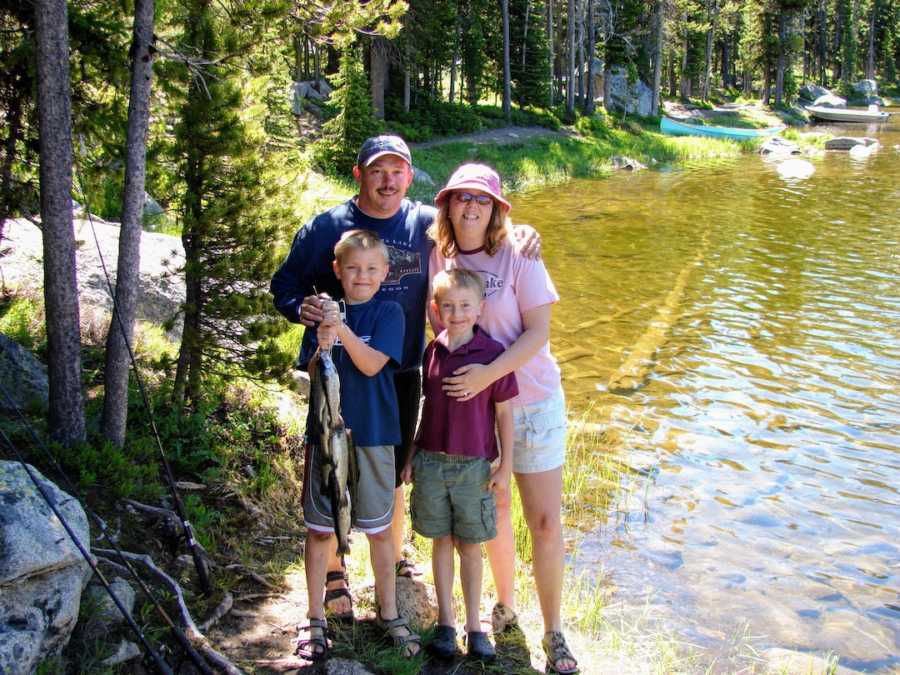 Family of four holding fish standing by creek