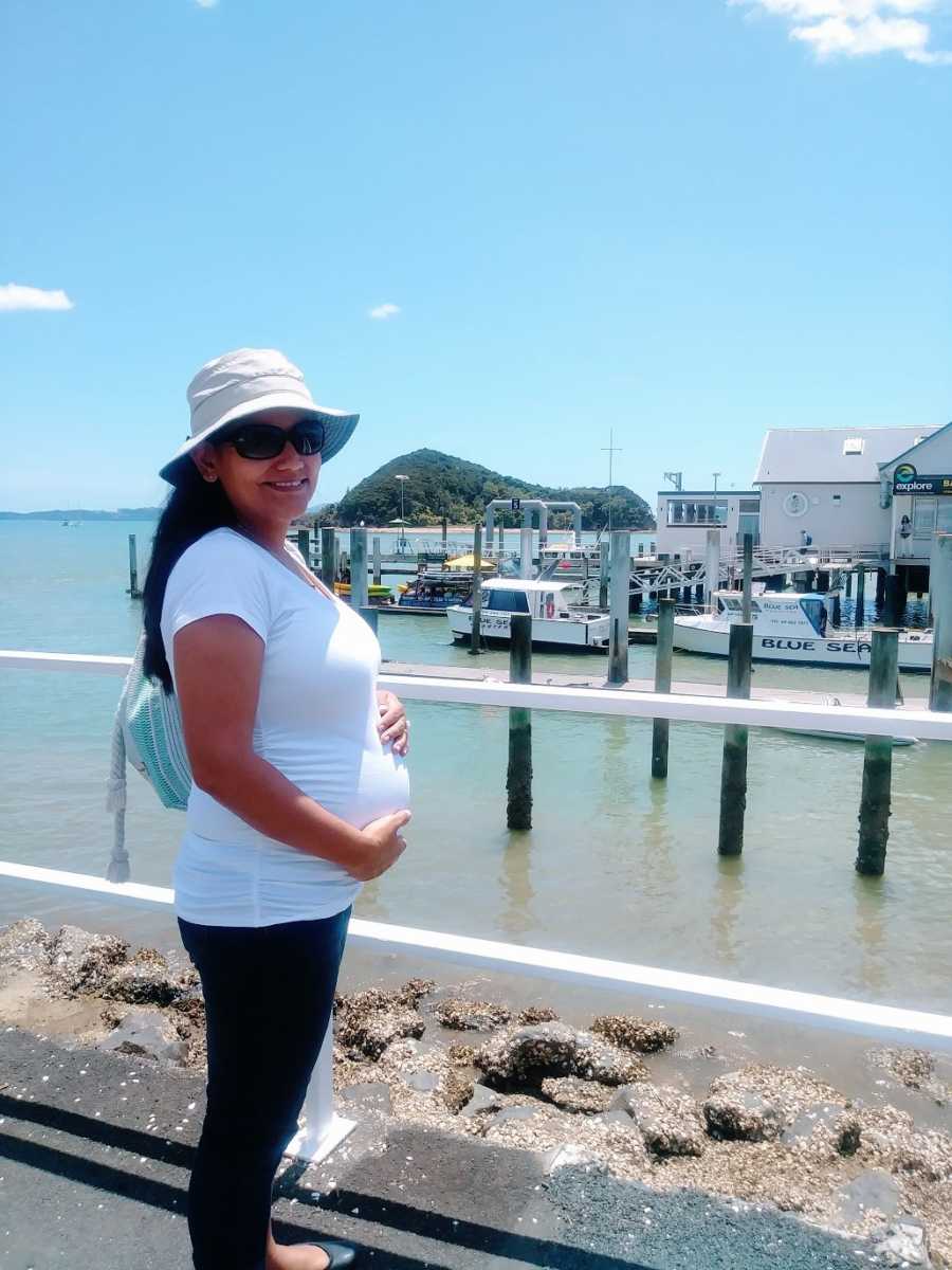 An expectant single mother by choice stands near a dock holding her baby bump