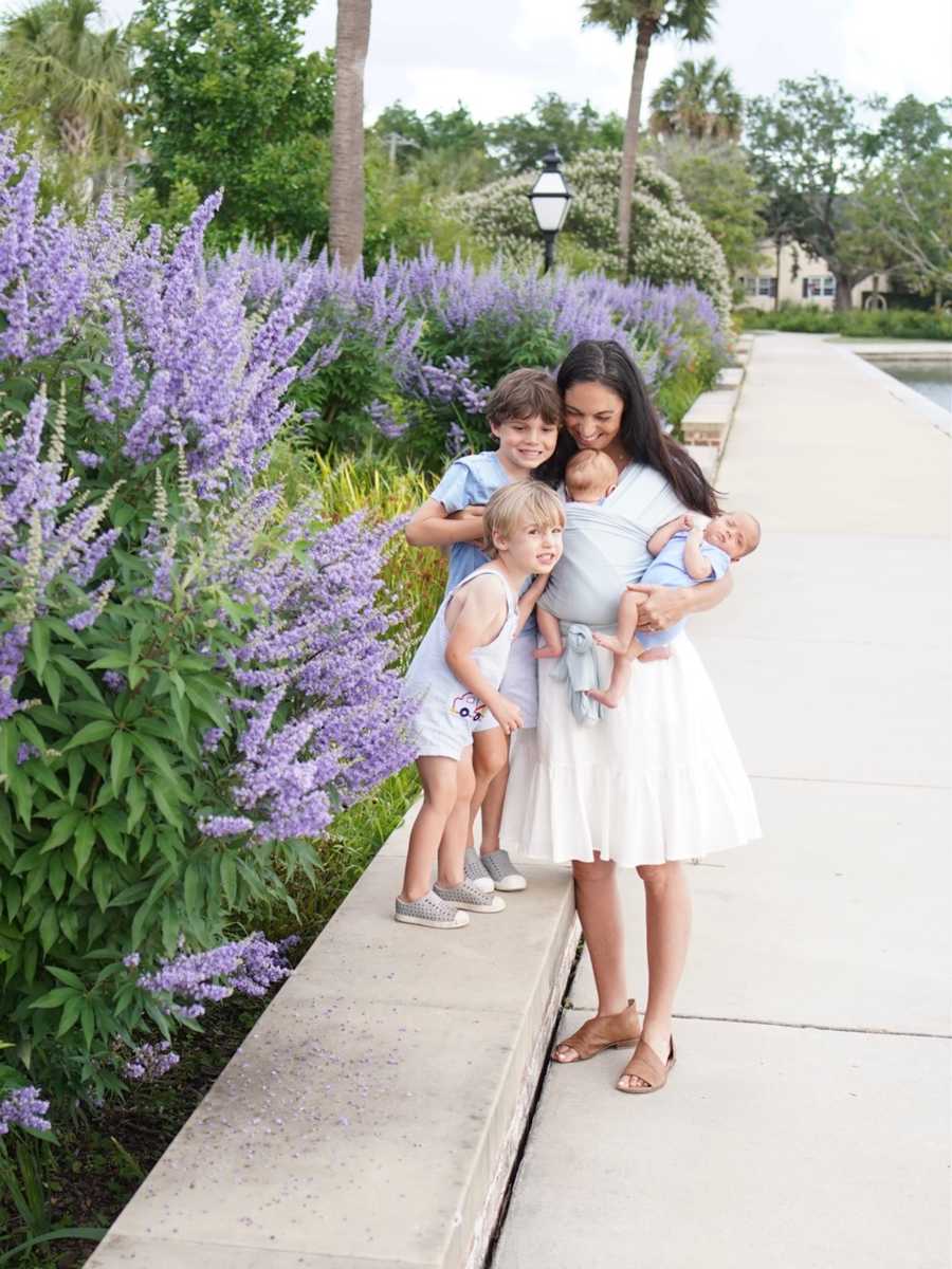 Pregnant mother holding all four children by purple flowers