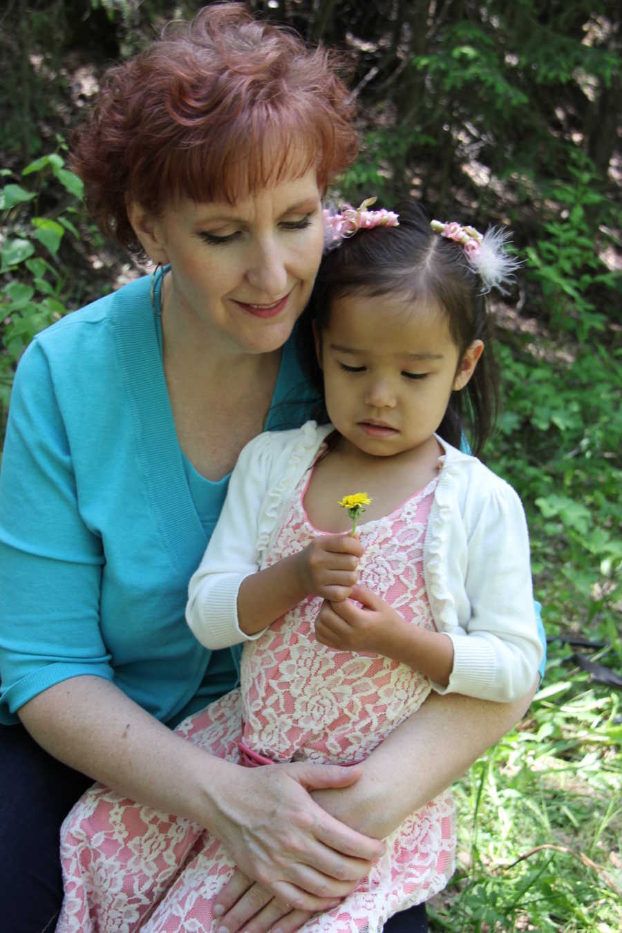 Mother and daughter sitting outside looking at dandelion