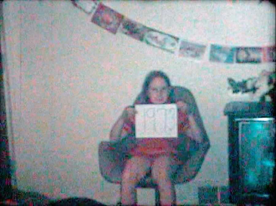 Old photo of young girl sitting in chair holding up paper
