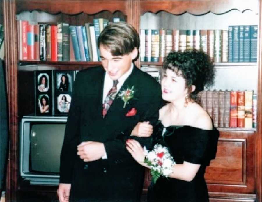 A girl with curly brown hair wears a black dress standing next to her prom date