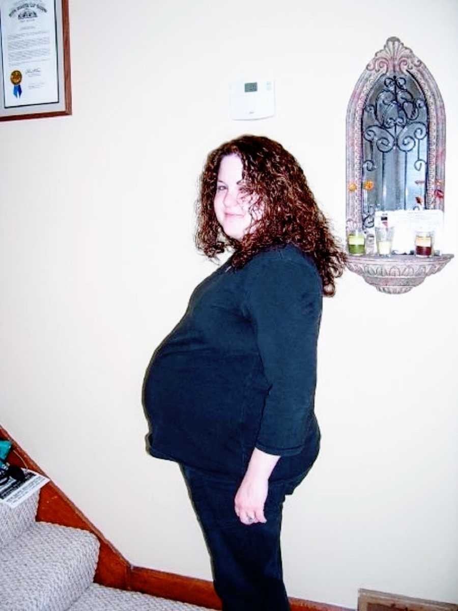 A woman with curly brown hair shows off her baby bump