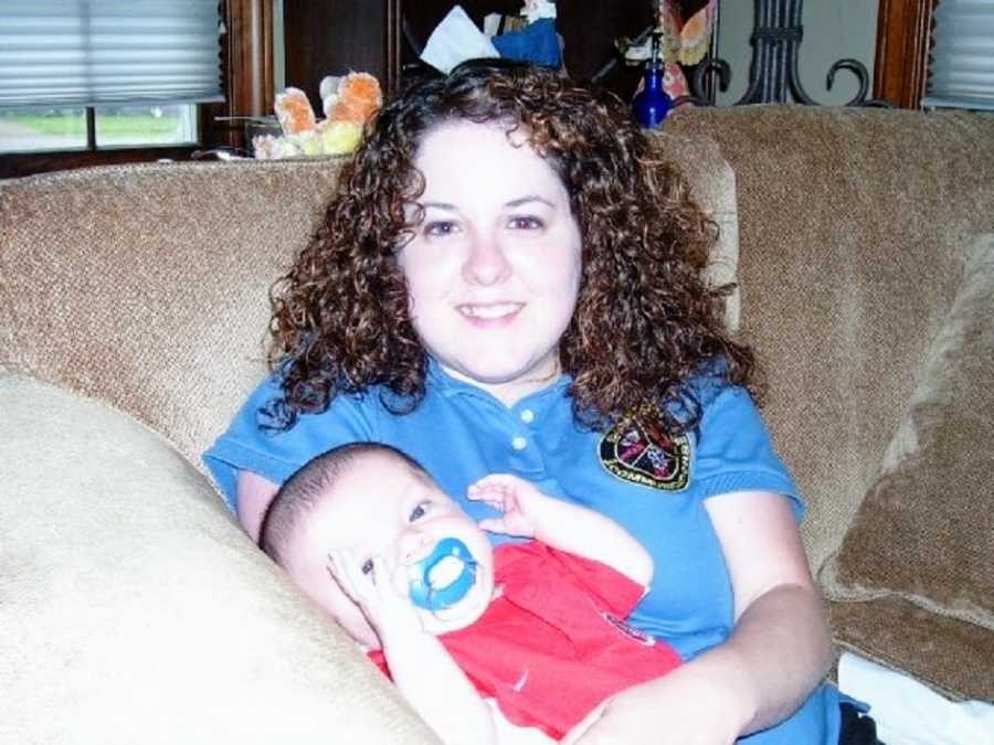 A mother with curly brown hair holds her young son on a couch