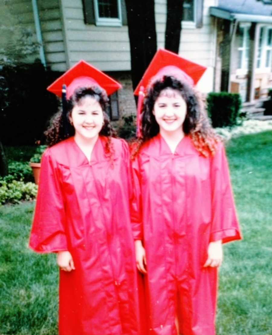 Twin girls with curly hair dressed in red caps and gowns for graduation