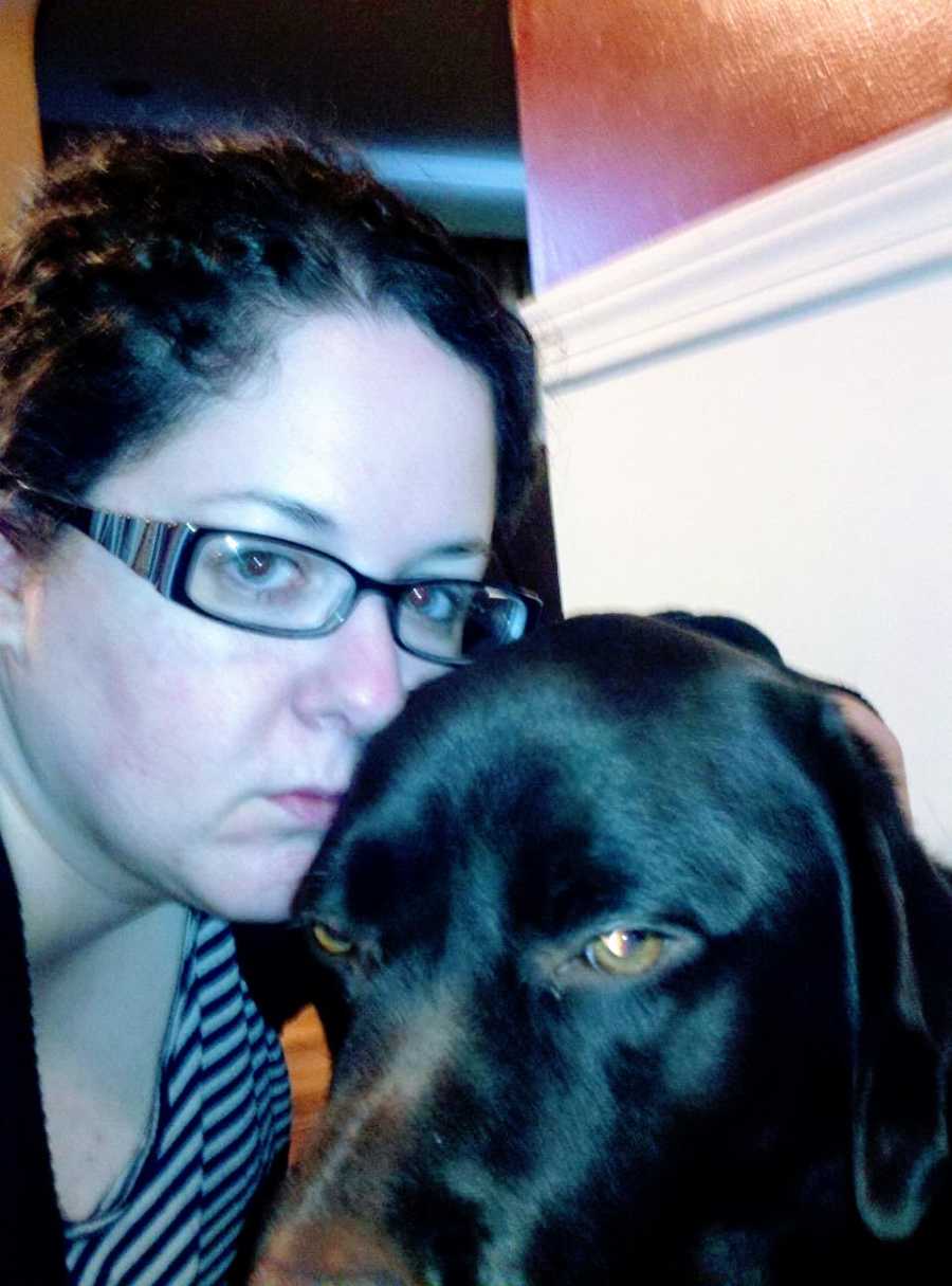 A woman who is struggling with her mental health sits next to a brown dog