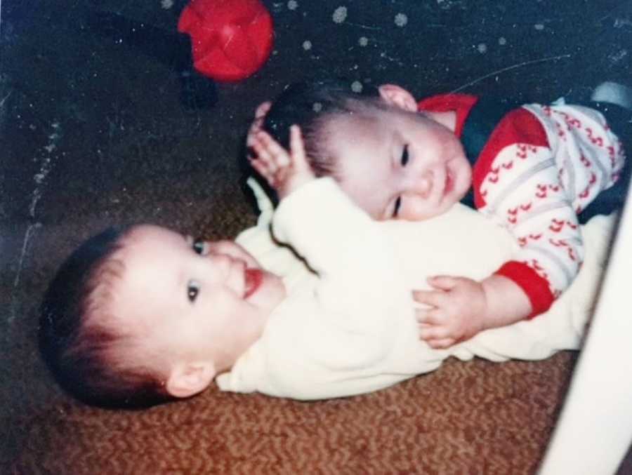 A toddler lies on top of her twin sister