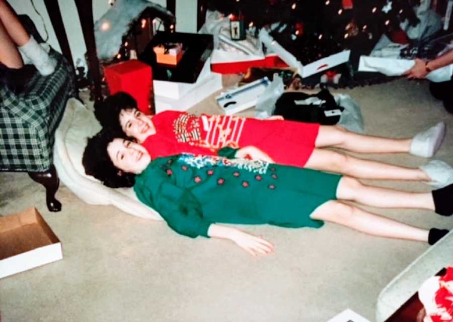 Twin girls lie on the floor together wearing Christmas clothing