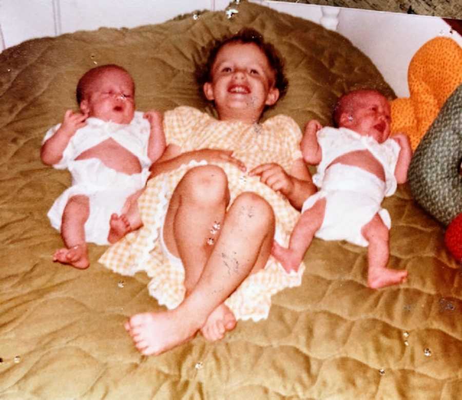 A girl lies on a bed with her baby twin sisters