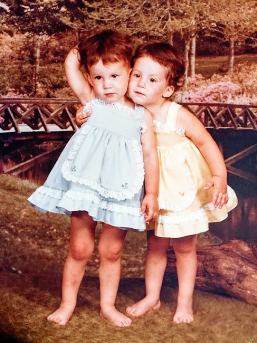 Twin girls wearing dresses hug each other