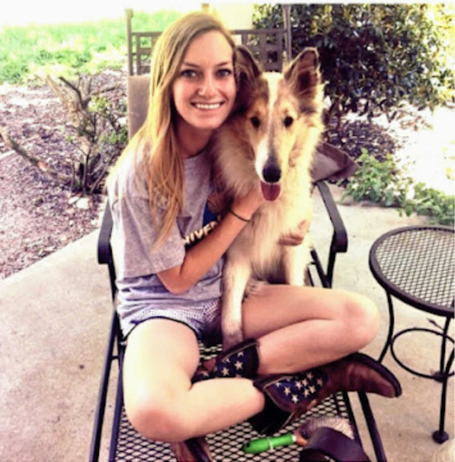 Young blonde woman sitting in metal chair outside on patio with dog