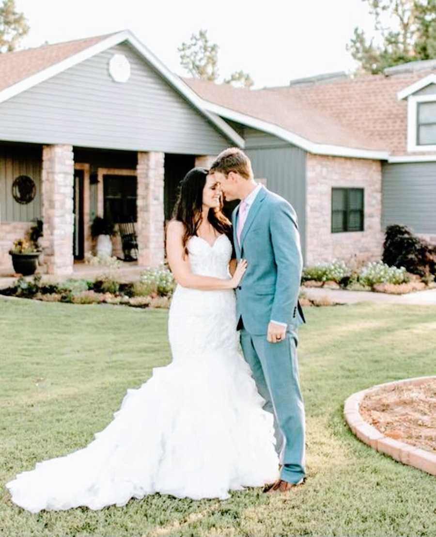 A bride and groom stand together outside their home