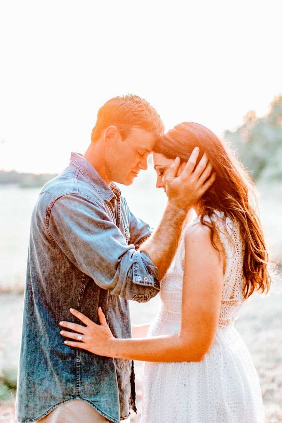 A man and his wife stand on a beach with their foreheads touching