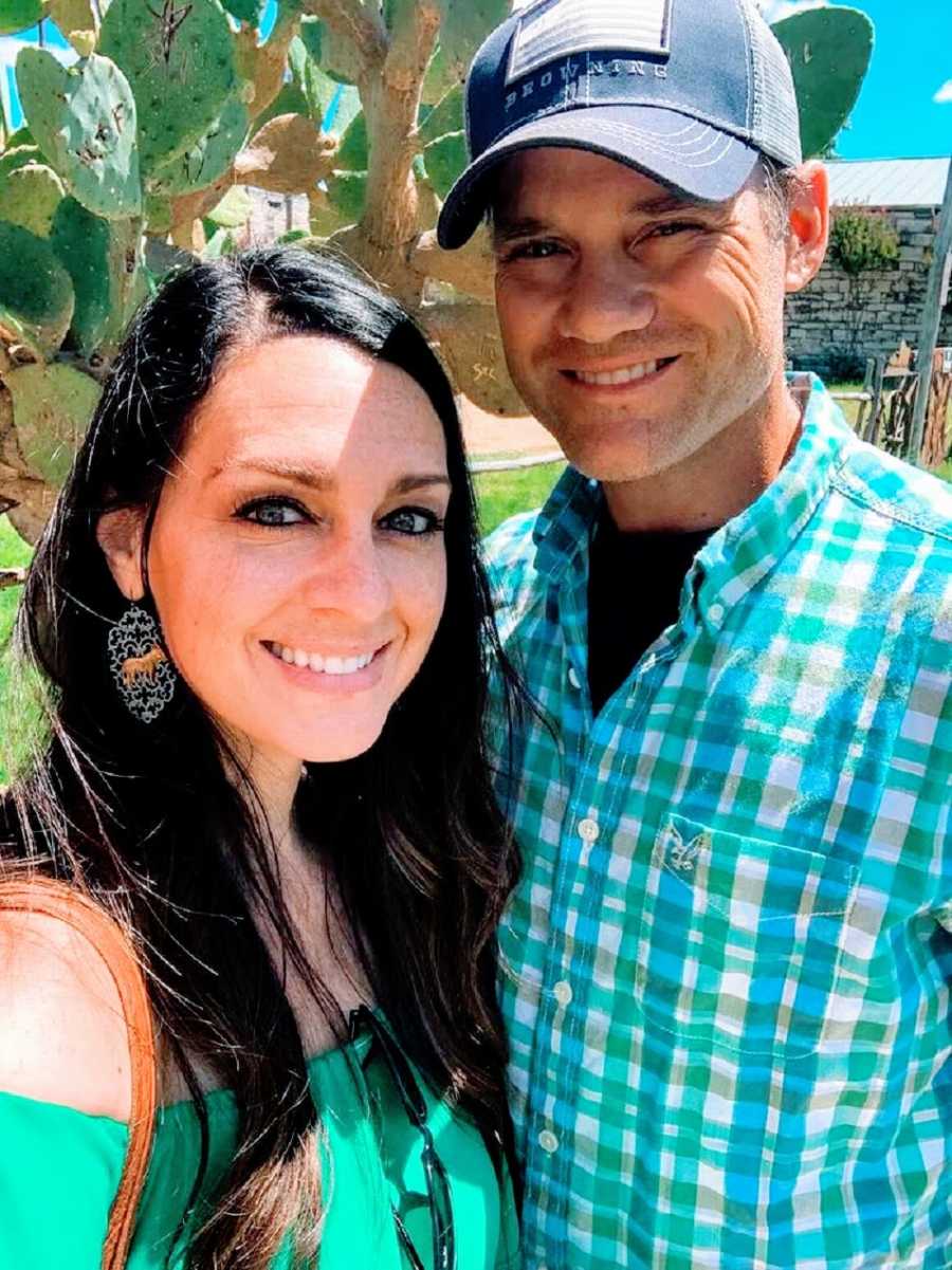 A husband and wife standing together near some plants