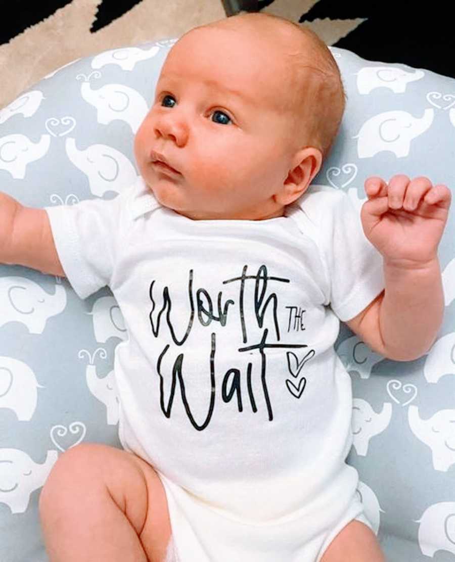A baby boy wears a shirt that says "Worth the Wait"