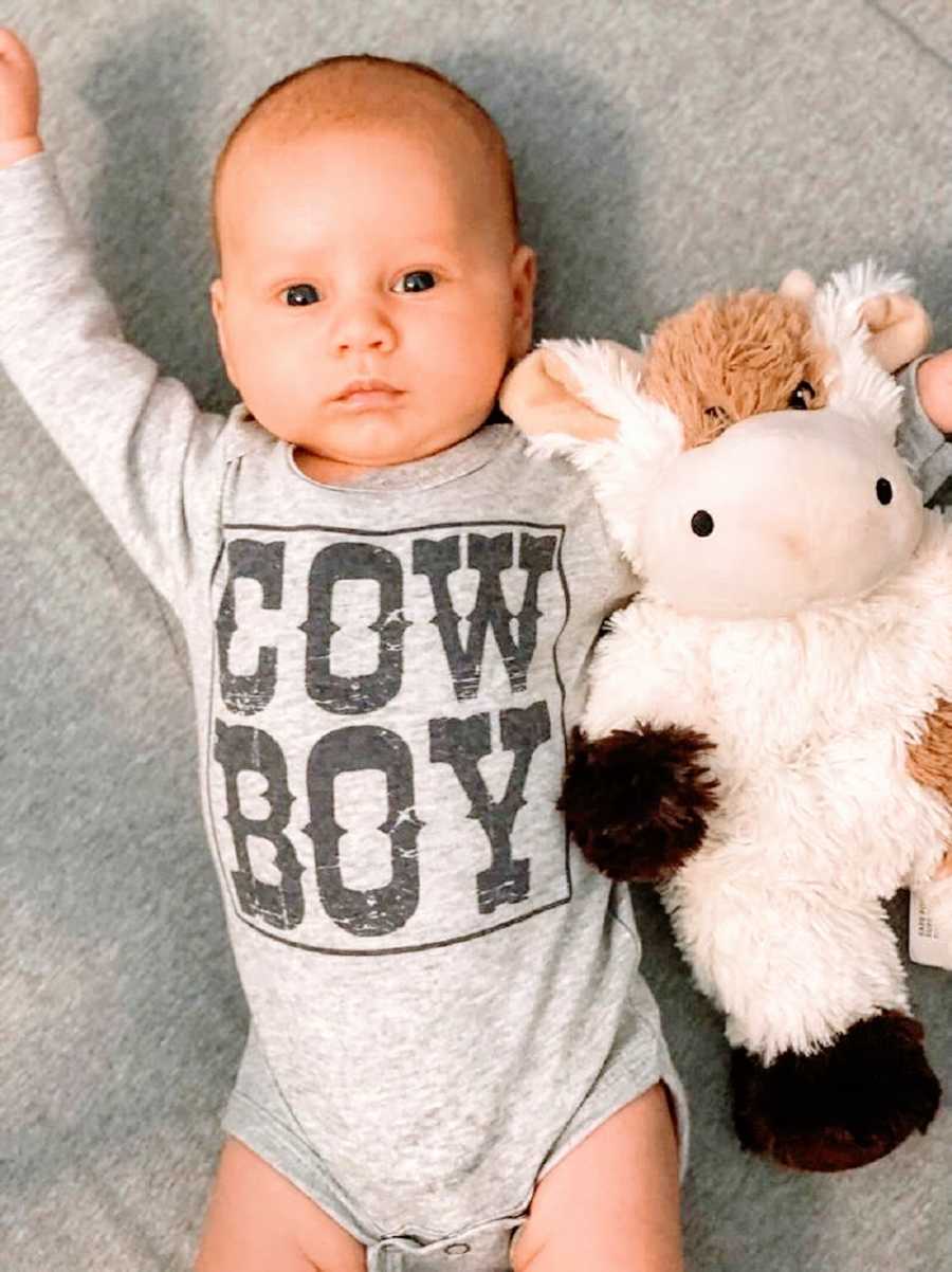 A baby boy wearing a shirt that says "Cowboy" holds a stuffed cow