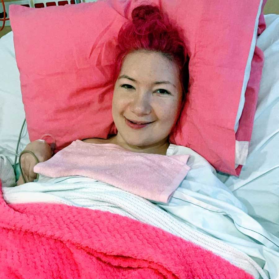 A woman with endometriosis lies on a pink pillow in a hospital bed