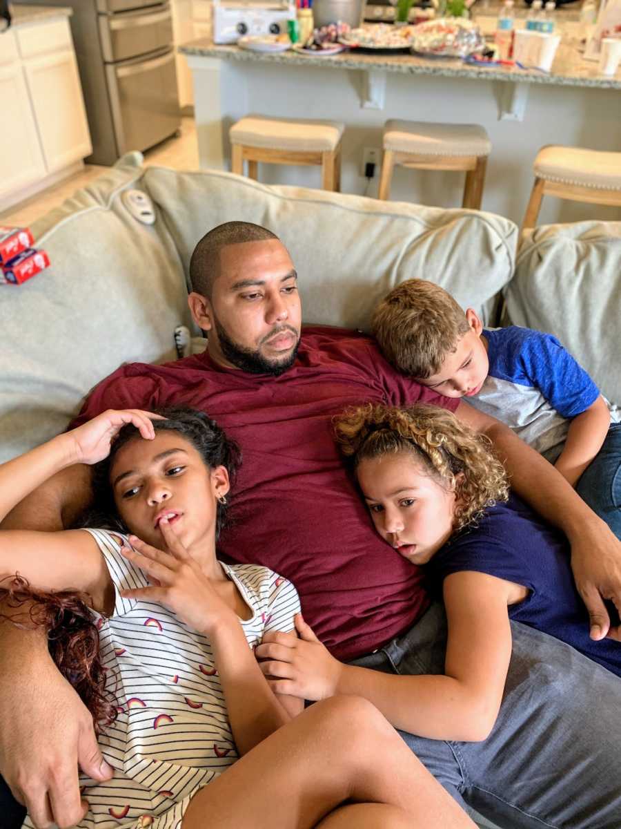 Father lying on couch cuddling with three children