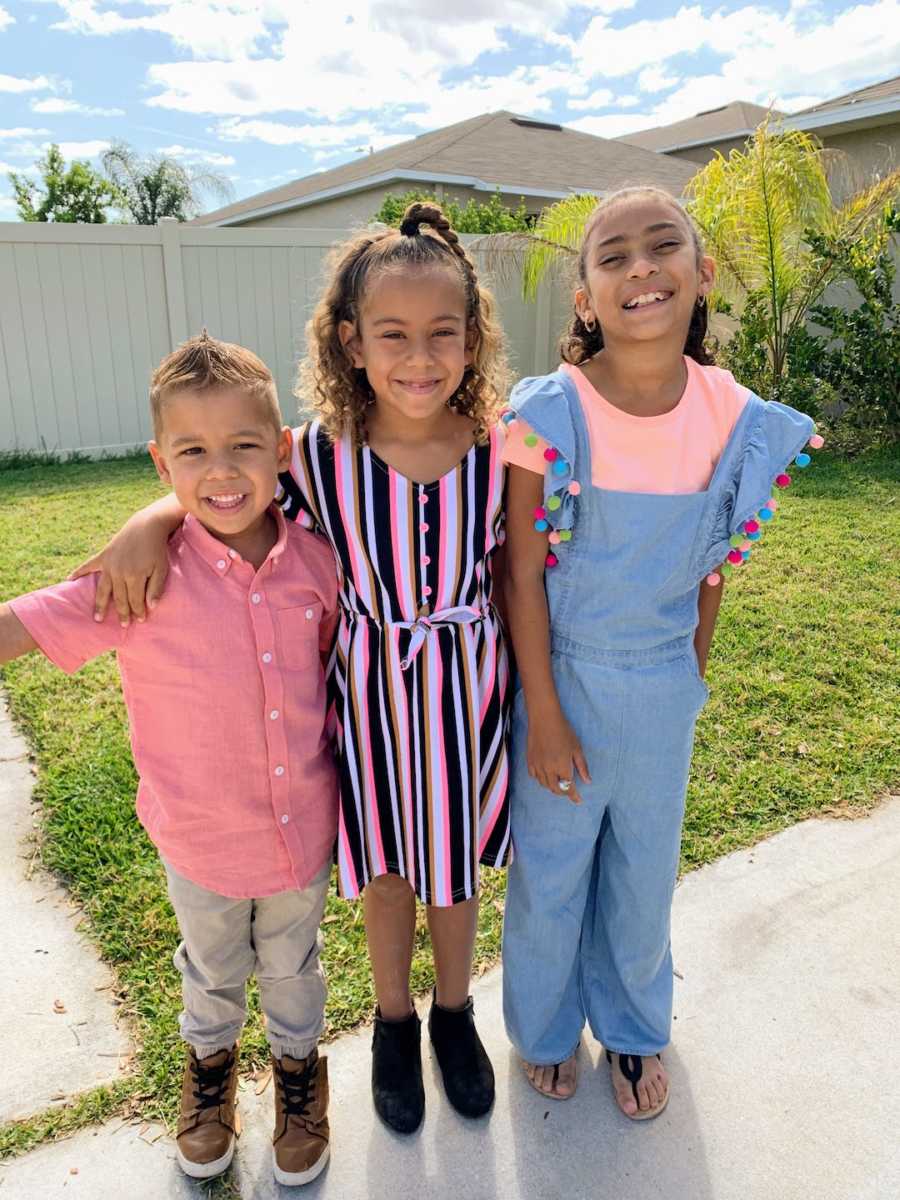 Two sisters standing with arms around their little brother outside