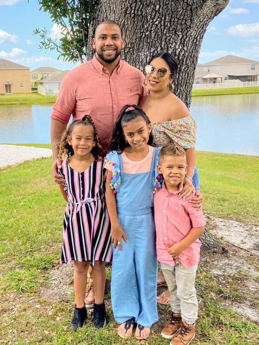 Blended family of 5 standing by tree with water in background