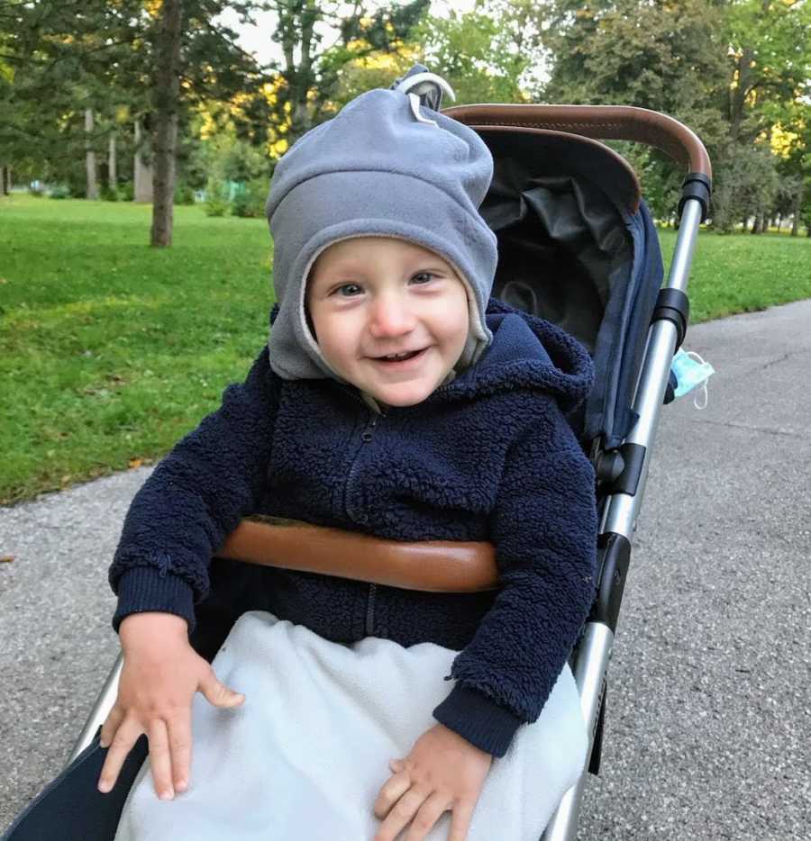 Toddler boy sitting in stroller wearing hat and smiling