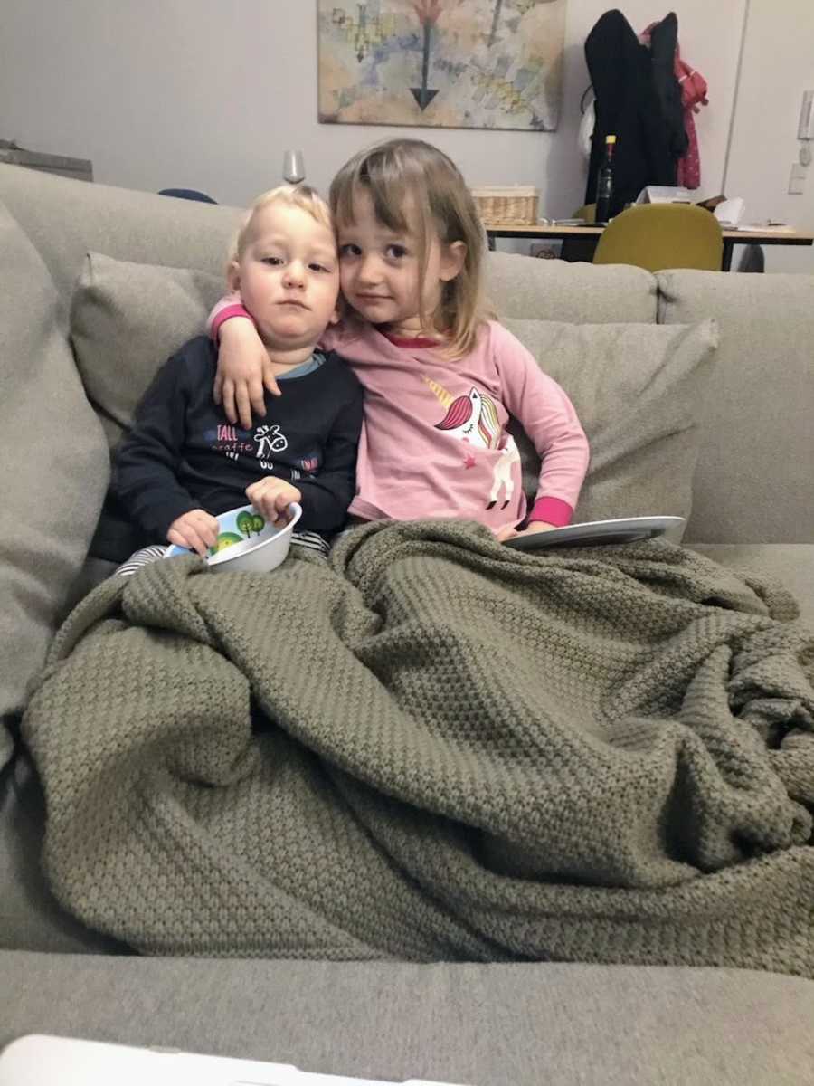 Brother and sister wrapped in blankets on brown couch