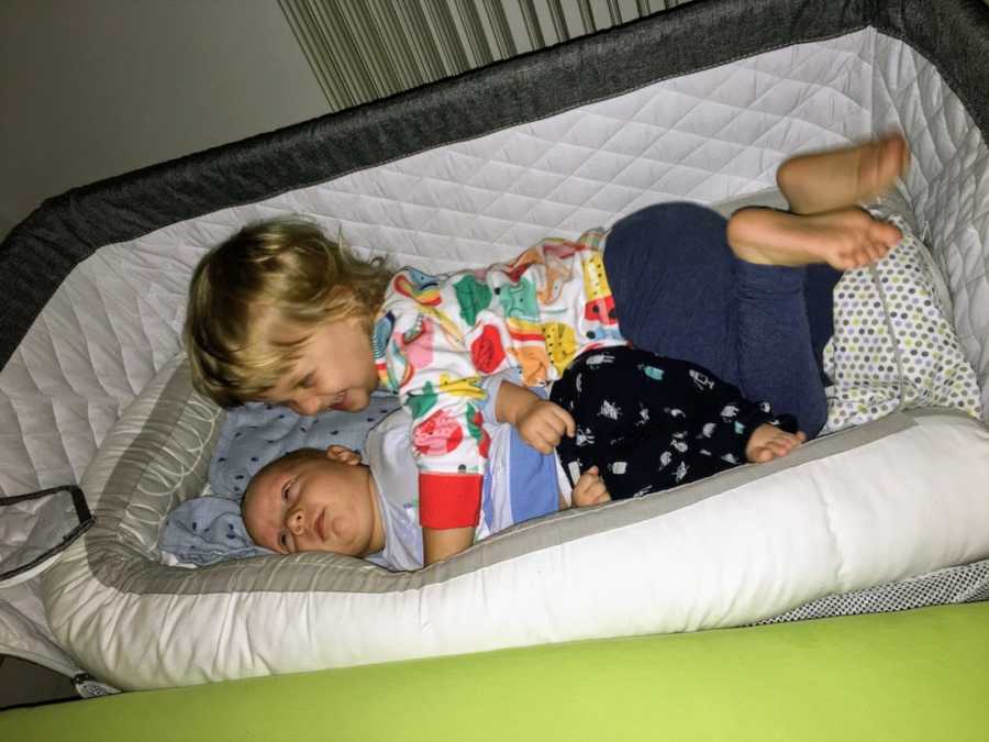 Newborn baby boy lying in crib with big sister
