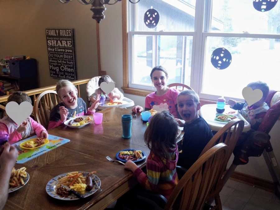 Large group of foster siblings sitting at kitchen table smiling