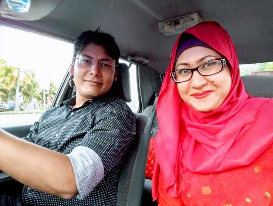 A woman in a red hijab and her husband sit in a car