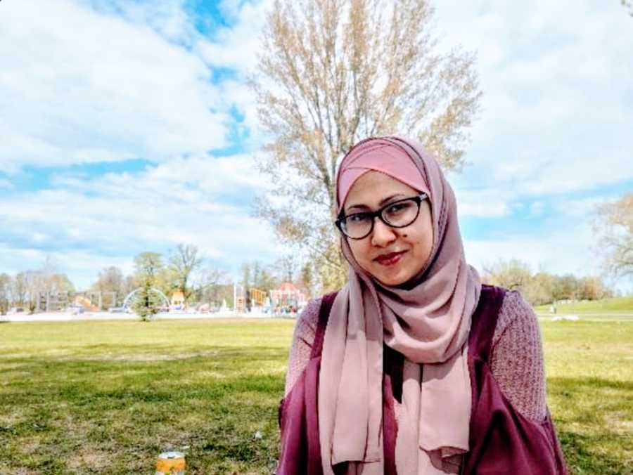 A neurodivergent mother wearing a hijab stands in a park