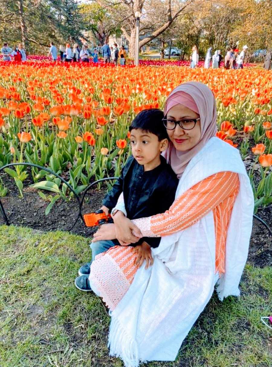 A neurodivergent mom holds her autistic son near flowers at a park