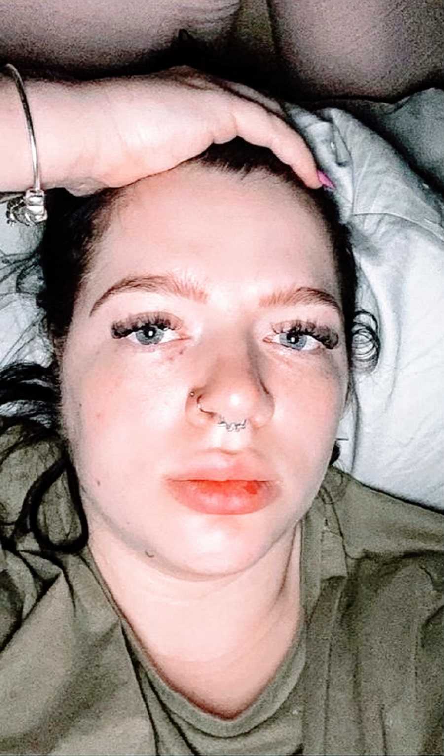 A woman with nose piercings lies uncomfortably in bed