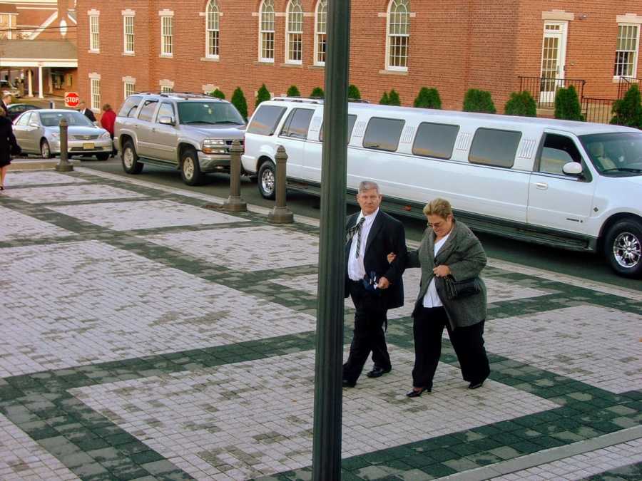 Brother and sister walking on street with white limo in background