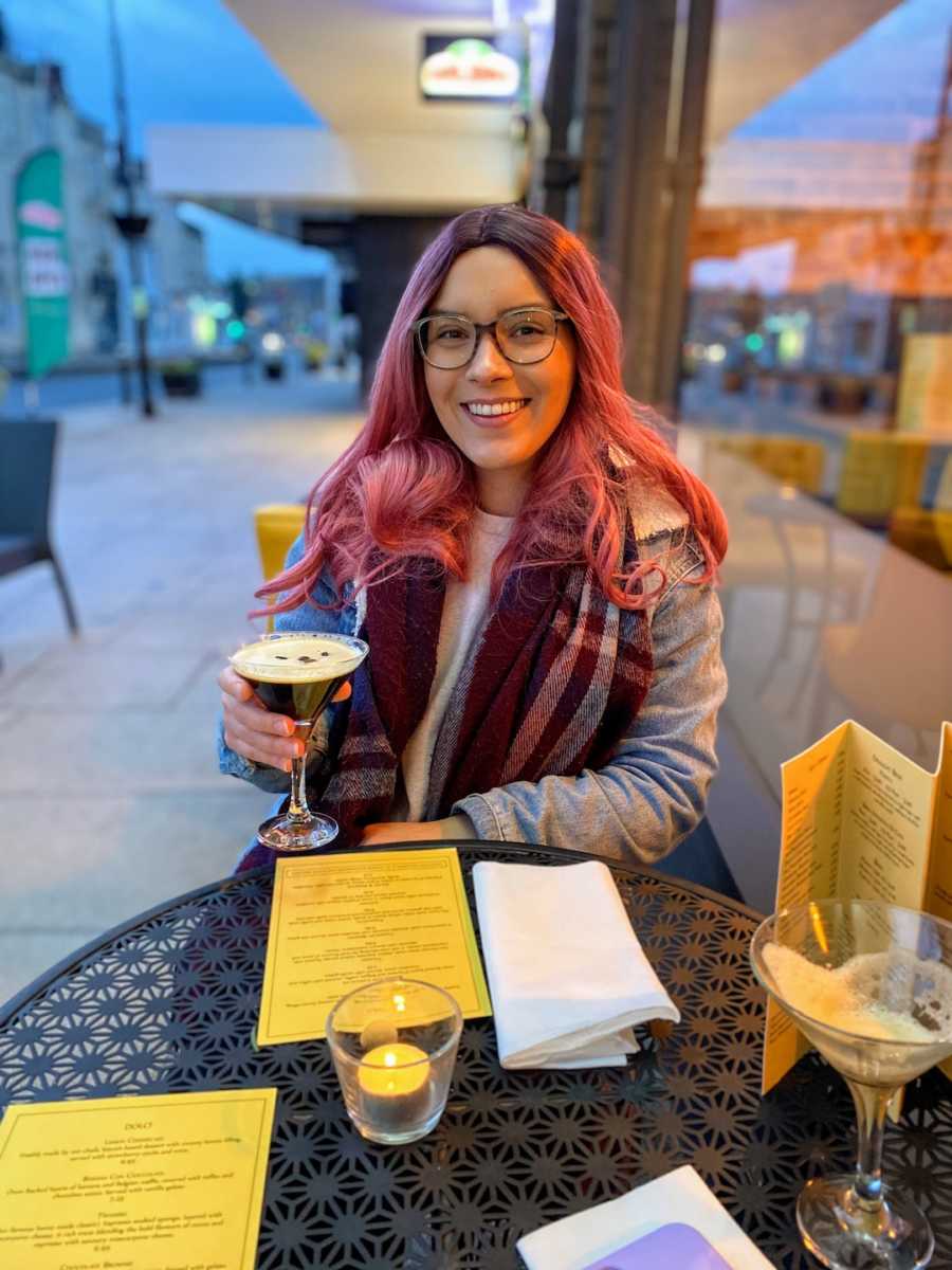 Woman wearing pink wig sitting at restaurant holding wine glass